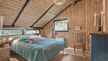 Ein Schlafzimmer mit Holzbalkendecke, einem Bett mit blauer Bettdecke, einem Sessel und einer Kommode.