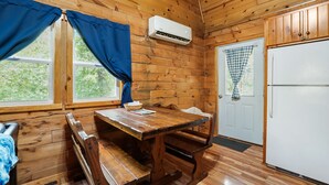 Une cabane en bois avec une table à manger, des bancs, un réfrigérateur et une fenêtre avec des rideaux.