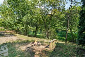 A campsite with a fire pit surrounded by trees, a wooden bench, and a clear sky.