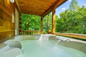 A wooden cabin with a hot tub under a wooden deck, surrounded by lush green trees. - Butterfly Crossing | Private Lake, Hot Tub (Logan)