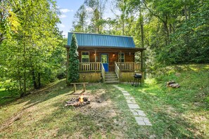 A cabin with a wooden deck, a fire pit, and a stone pathway leading to the entrance. - Butterfly Crossing | Private Lake, Hot Tub (Logan)