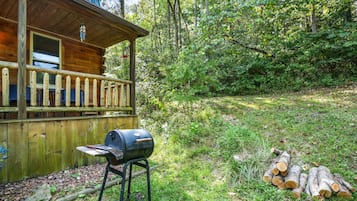 Eine Holzhütte mit Veranda, Grill und Holzstoß.
