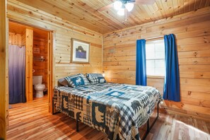 A wooden cabin bedroom with a bed, a window with curtains, a ceiling fan, and a framed picture on the wall. - Butterfly Crossing | Private Lake, Hot Tub (Logan)