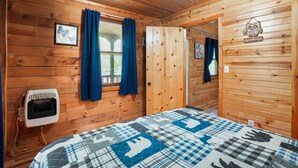 Une pièce de cabane en bois comprenant un lit, un radiateur et une porte donnant sur une autre pièce.