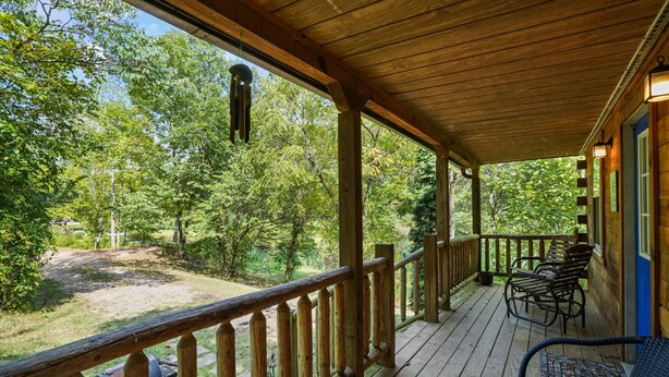 Une terrasse en bois avec une rambarde, des meubles d’extérieur et une vue sur une zone boisée.