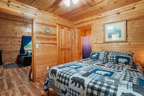 Un dormitorio de cabaña de madera con una cama, una puerta que da a otra habitación y un cuadro enmarcado en la pared.
