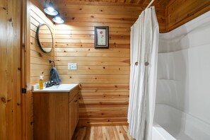 A wooden-paneled bathroom with a sink, mirror, and framed picture on the wall.