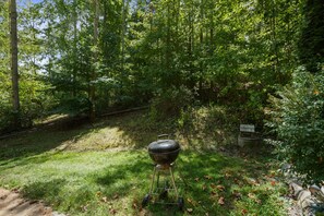 Un barbecue portable installé dans une zone boisée, à proximité d’un repère en pierre et d’un sentier.