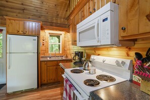 A kitchen with wooden cabinets, a white refrigerator, a microwave, a stove, and a coffee maker. - Fireflies Hollow | Romantic Pond Retreat, Hot Tub (McArthur)