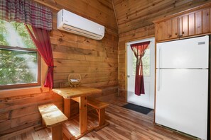A wooden cabin interior with a wooden table, bench, white refrigerator, and an air conditioning unit.
