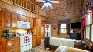 A cabin interior with wooden walls, a kitchenette, a sofa, and a television. - Fireflies Hollow | Romantic Pond Retreat, Hot Tub (McArthur)