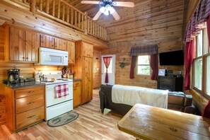 A cabin interior with wooden walls, a kitchenette, a sofa, and a television. - Fireflies Hollow | Romantic Pond Retreat, Hot Tub (McArthur)