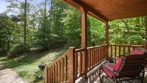 A covered wooden deck with a view of a forest. - Fireflies Hollow | Romantic Pond Retreat, Hot Tub (McArthur)