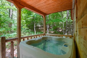 A hot tub in a wooden cabin with a wooden deck and a forest view.
