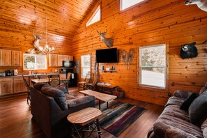 A log cabin interior with a dining area, sofa, television, and mounted animal heads.