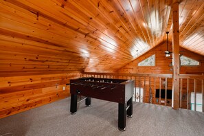 Ein Zimmer mit Holzboden, einem Kicker, einem Fernseher und einem Fenster.