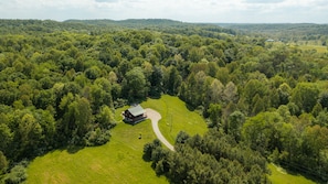 Eine Vogelperspektive auf ein ländliches Anwesen mit einem großen Haus, umgeben von dichtem Wald, einer kurvenreichen Auffahrt und blauem Himmel.