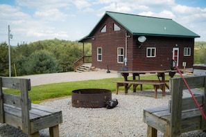A rustic cabin with a green roof, a fire pit, wooden benches, and a picnic table. - Golden Ridge | Hocking Hills, 62 Acres, Hot Tub (Logan)