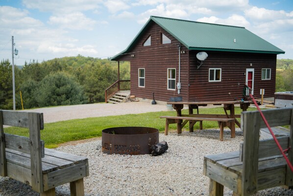 Une cabane rustique avec un toit végétalisé, un foyer, des bancs en bois et une table de pique-nique.