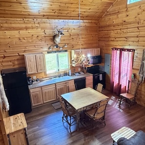 Ein Blockhaus-Interieur mit Holzwänden, einem Esstisch mit Stühlen, einer Küchenzeile und einem aufgehängten Hirschkopf.