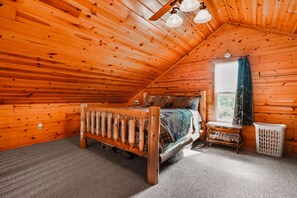 Une pièce de cabane en bois comprenant un lit, une fenêtre avec des rideaux, une petite table et un radiateur.