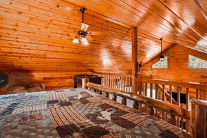 Ein Holzblockhaus-Interieur mit Bett, Deckenventilator und Fenster.