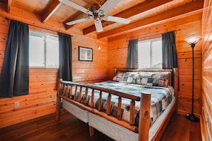 A wooden cabin bedroom with a bed, ceiling fan, and windows. - Golden Ridge | Hocking Hills, 62 Acres, Hot Tub (Logan)
