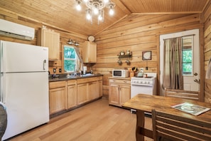 A wooden cabin kitchen with a refrigerator, microwave, stove, and wooden cabinets.