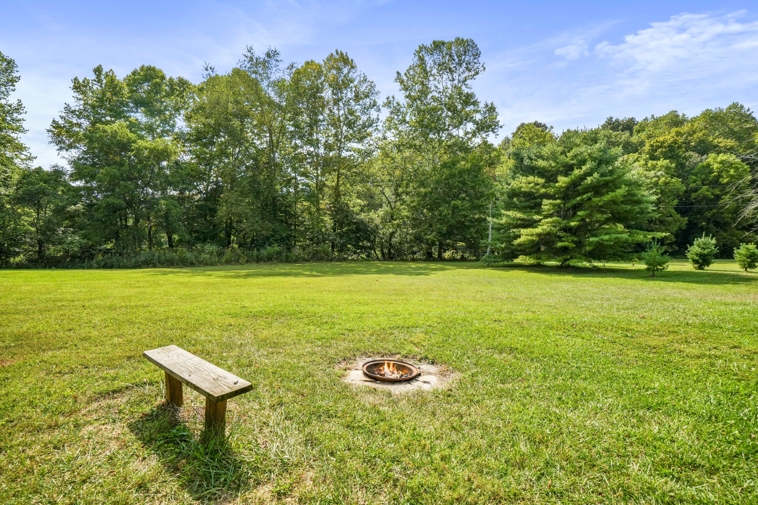 A grassy field with a fire pit and a wooden bench.