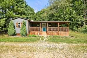 A cabin with a front porch, a small attached shed, and a stone pathway leading to the entrance.