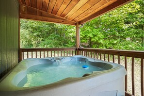 A hot tub under a wooden deck with a view of a forest.