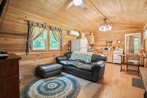 A cozy cabin interior with a wooden interior, a leather sofa, a dining table, and a kitchen area.