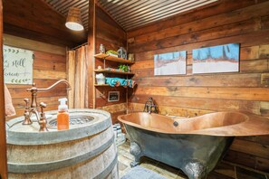 A rustic bathroom with a wooden interior, a clawfoot bathtub, and a vintage sink.