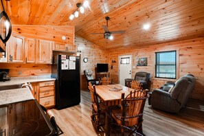 A wooden cabin interior with a kitchen, dining area, and seating.