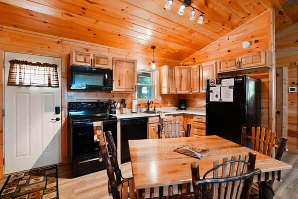 A wooden cabin interior with a kitchen, dining area, and a door with a window.