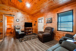 A log cabin interior with a television, a recliner, a sofa, and a wooden ceiling.