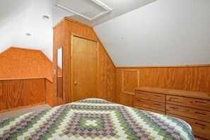 A bedroom with a wooden wardrobe, a bed with a patterned quilt, and a sloped ceiling.