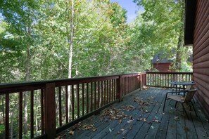 A wooden deck with a railing, a table, and chairs, surrounded by trees.