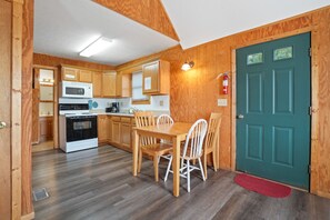 A compact kitchen with wooden cabinets, a microwave, stove, and a dining table with chairs.