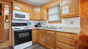 A kitchen with wooden cabinets, a white stove, a microwave, and a coffee maker. - Retreat Cabin #2 | Hocking Hills,  Pet Friendly (Logan)