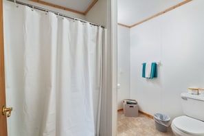 A bathroom with a shower curtain, a toilet, a trash bin, and two towels hanging on the wall. - Retreat Cabin #8 | Hocking Hills, Fire Ring (Logan)