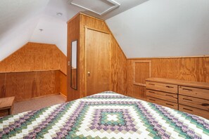 Un dormitorio con un armario de madera, una cama con colcha estampada y techo inclinado.