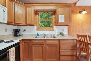 A kitchen with wooden cabinets, a double sink, a stove, and a window with a view of trees.