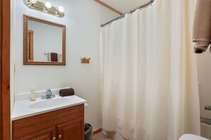 A bathroom with a wooden vanity, a mirror with lights, a white sink, and a shower curtain.
