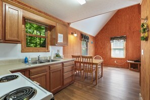 Une cuisine avec des meubles de rangement en bois, une cuisinière, un évier et un coin repas comprenant des chaises et une table.