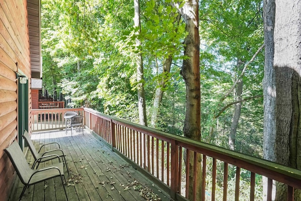 A wooden deck with metal chairs and a table, surrounded by tall trees.