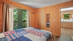 Un dormitorio con una cama grande, paredes de madera, una puerta verde y vistas al exterior.