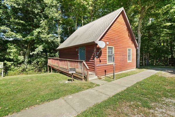 A small, single-story log cabin with a porch and a satellite dish.