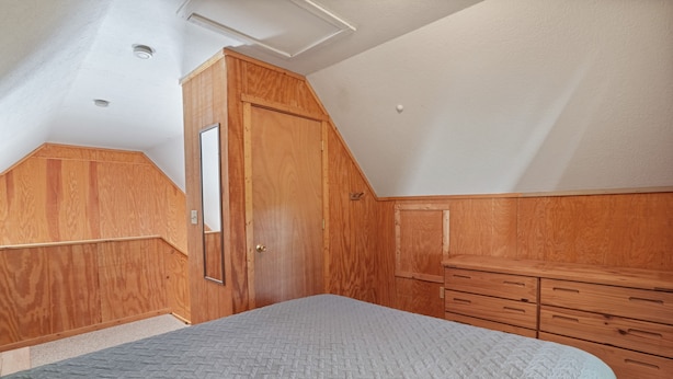 Un dormitorio con techo inclinado, armario de madera y cama con cubrecama acolchado.
