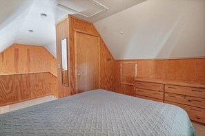 A bedroom with a sloped ceiling, wooden wardrobe, and a bed with a quilted cover.